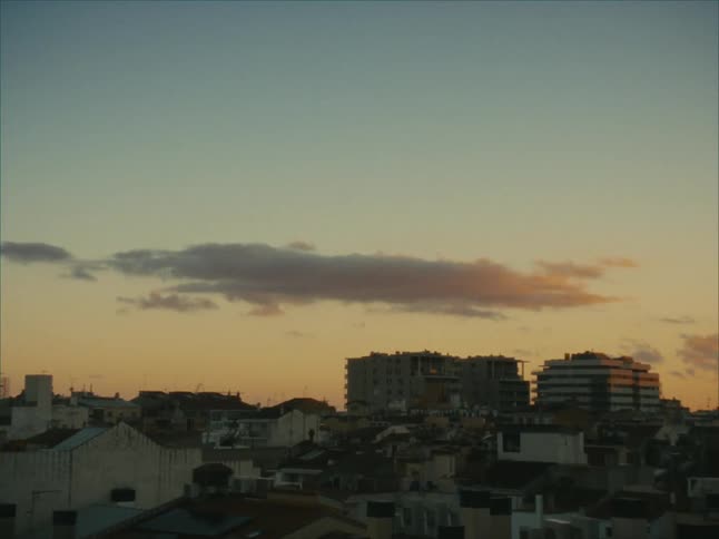 A single cloud lingers in a soft golden sunset over a cityscape