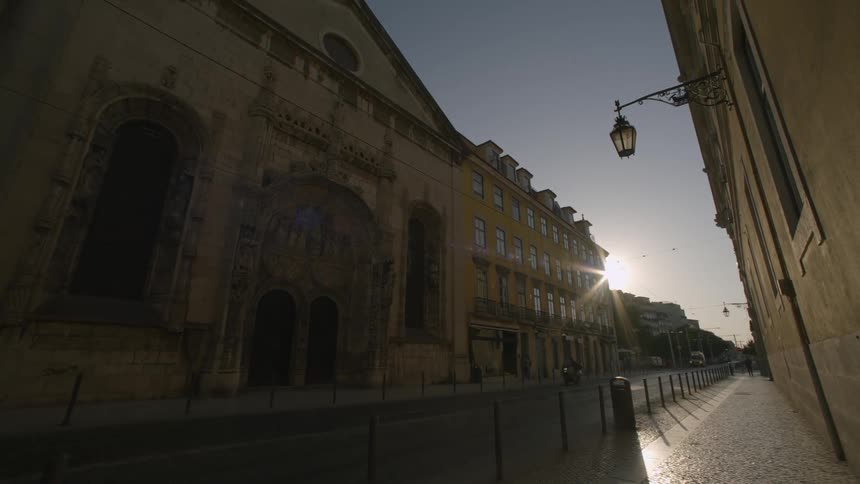 View of a street with buildings on one side and the sun casting a warm glow and long shadows