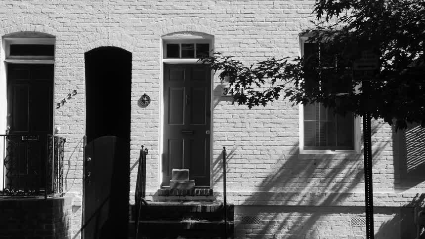 The facade of a brick building with a thin wooden door and an external staircase and everything is in black and white tones