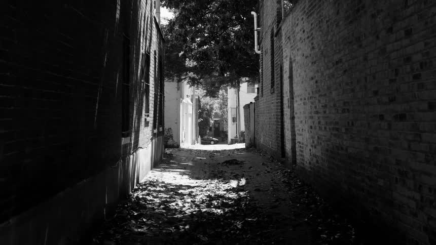 Narrow alleyway flanked by brick walls with sunlight filtering through at the far end