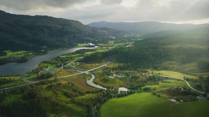 Aerial landscape of rural areas between hills with river and surrounded by mountains with sun on horizon
