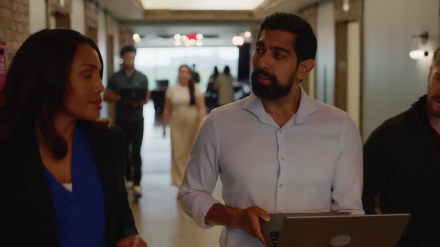 Three coworkers collaborate around a laptop while walking down a hallway