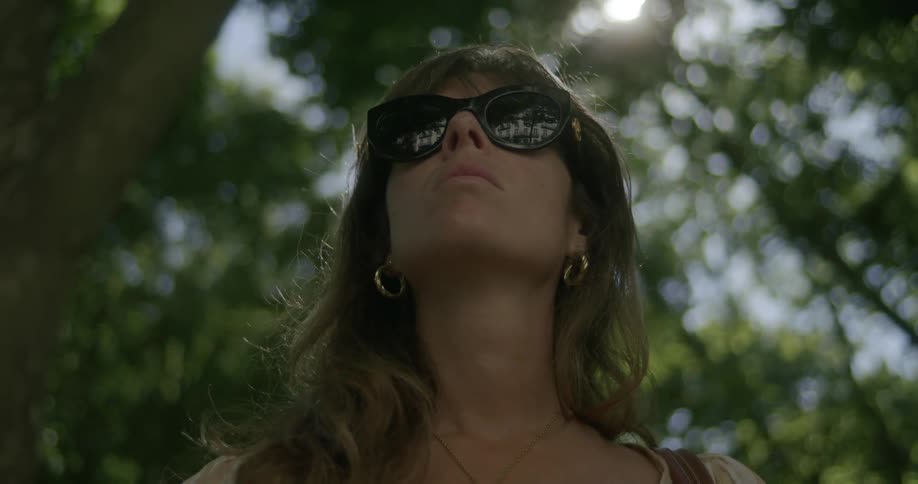 Woman with black sunglasses under a tree looking around