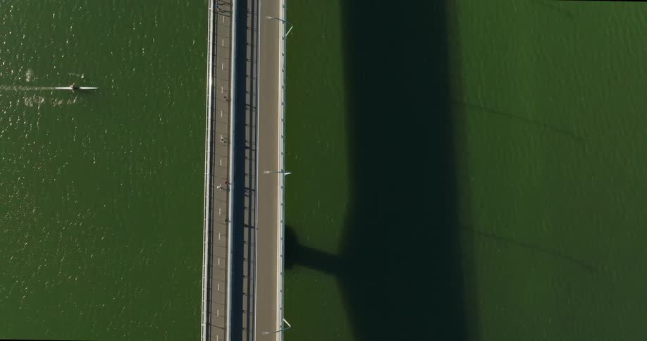 A suspension bridge over water with a street and a walkway for people to walk on seen from above