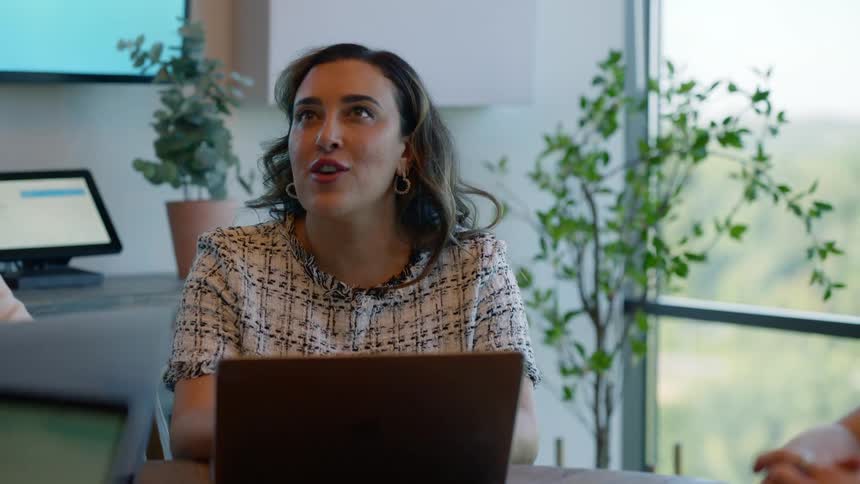 Woman with laptop at desk chatting happily with her coworkers
