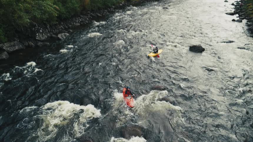 Two people in kayaks navigate through river rapids