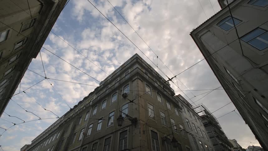 View of the sky between two tall buildings focusing on the corner of an aging building with several windows