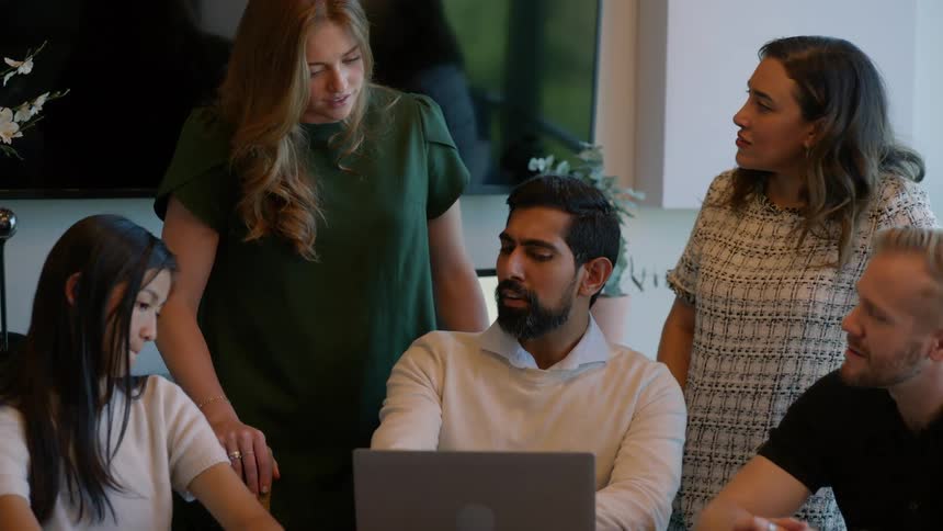 Group of people talking in an office around a laptop