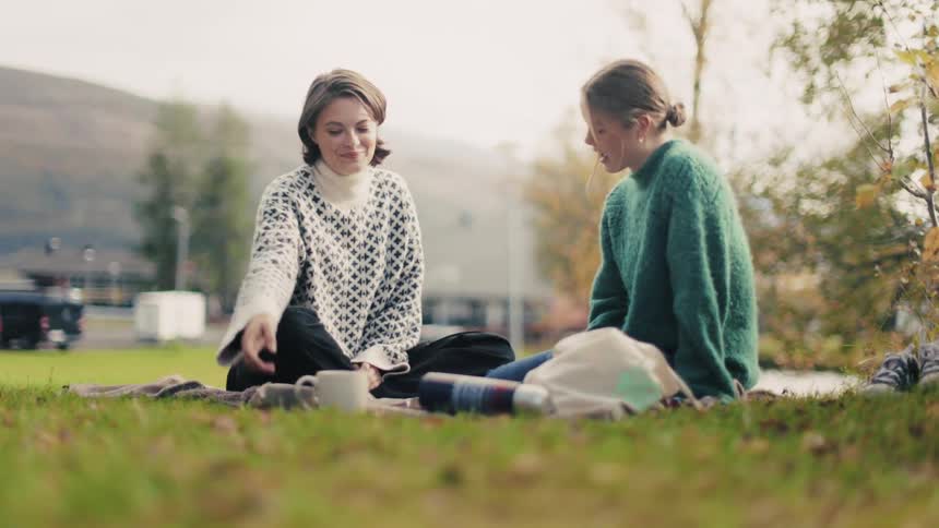 Friends enjoying a picnic on a hillside drinking hot beverages
