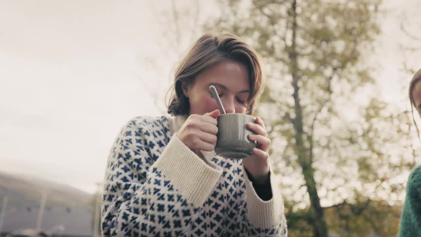 Two women in an outdoor space talking and smiling with one of them drinking from a mug