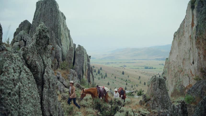 Man and a woman each walking beside a horse up a hill on a cloudy day
