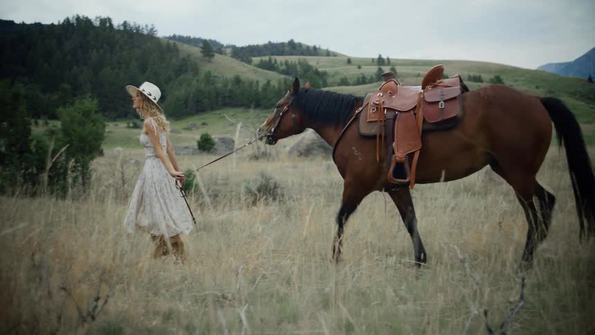 Woman walking in a field and pulling a brown horse