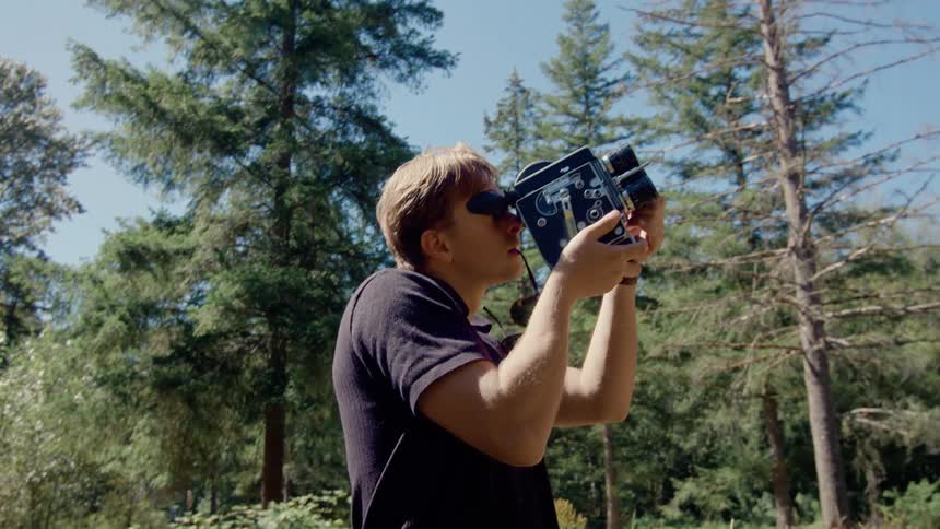 A white man uses an old film camera to shoot footage in nature
