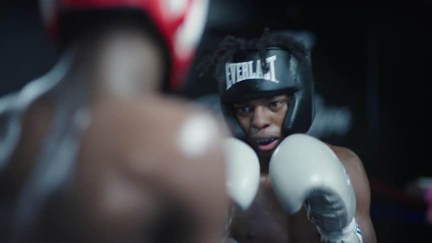 Two young men are boxing with each other while wearing gloves and headgear
