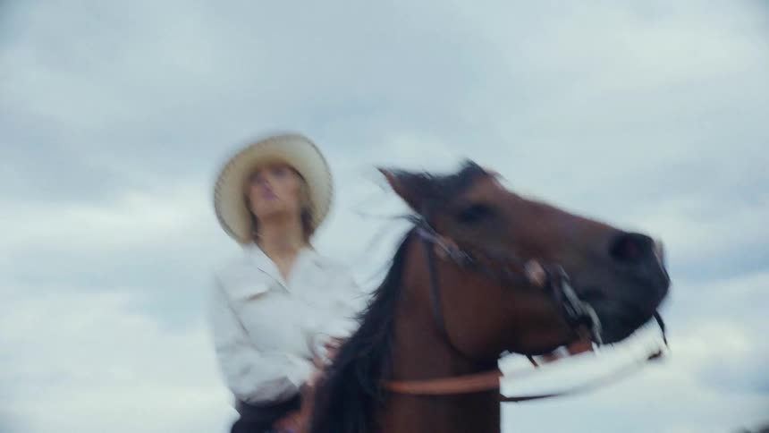 Woman rides a horse across a high field overlooking a valley on a hazy day
