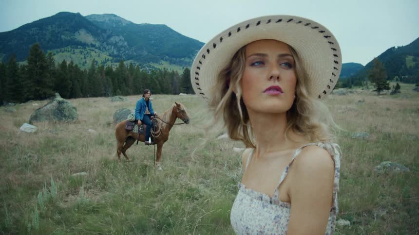 A man an woman on horseback look around their rural surroundings