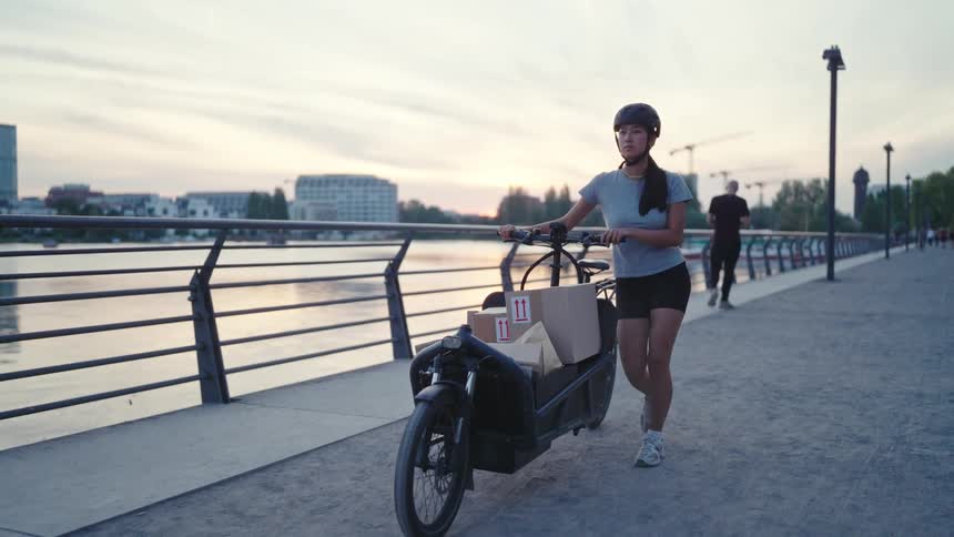A woman in a helmet walks alongside her cargo bike while pushing it