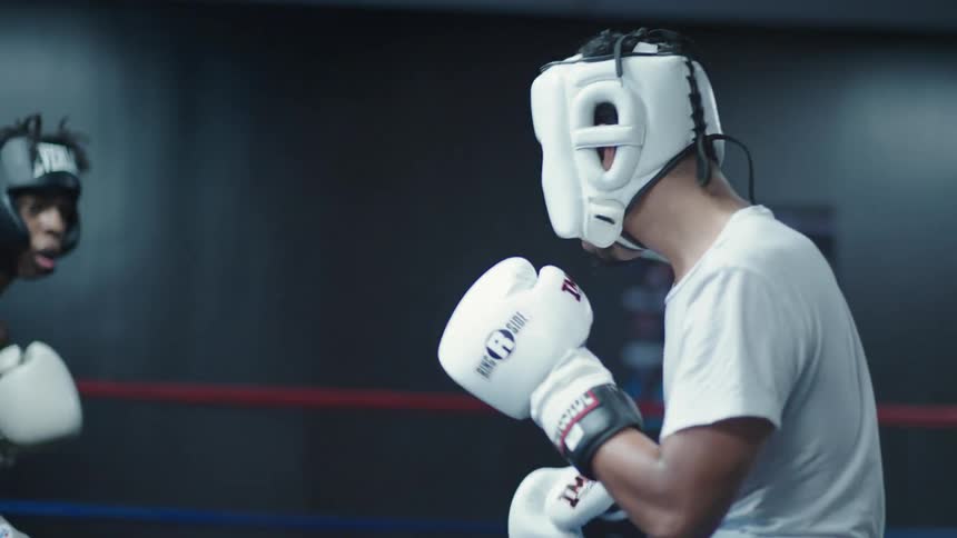Two men in protective helmets boxing and a person watching