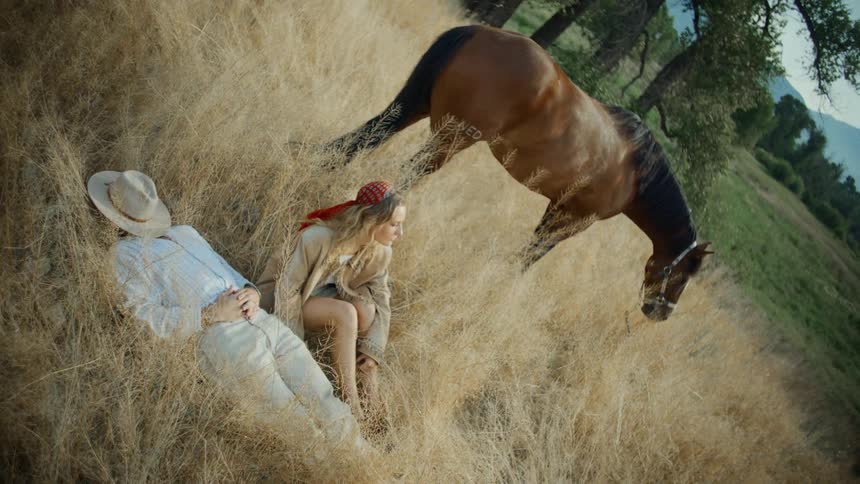Two individuals resting next to a horse in a field with tall dry grass