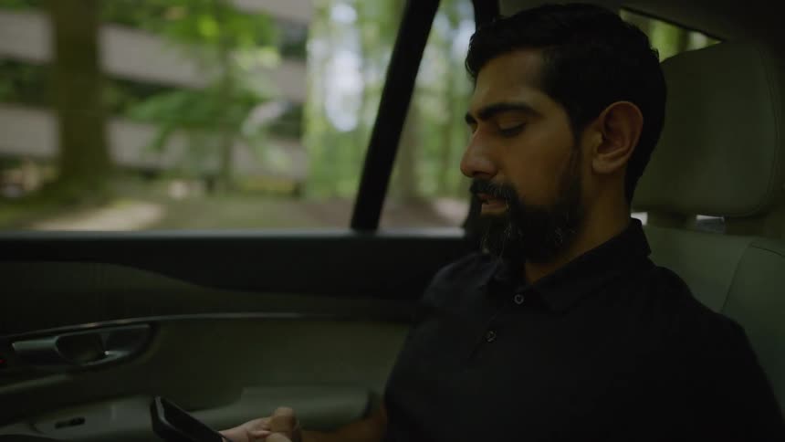 A bearded man riding in a car texts on his smartphone