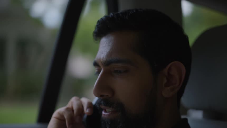 A man laughs as he speaks on a phone while driving through a suburb