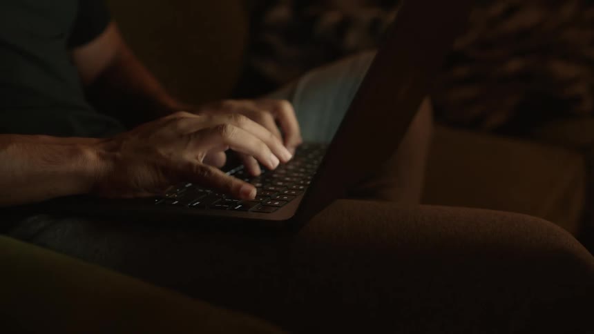 A person sits with their laptop while typing using its keyboard