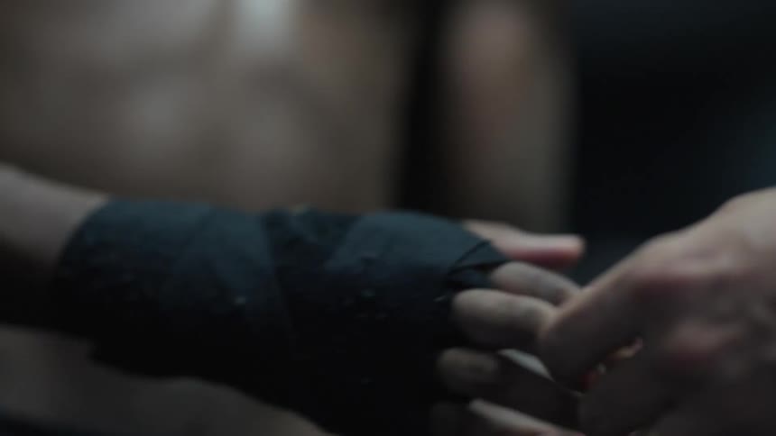 The coach helps the boxer wrap his hands in black bandages
