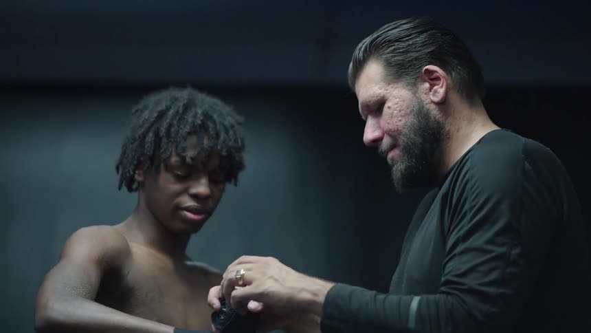 Man placing a black belt on a teenagers hand inside a boxing ring