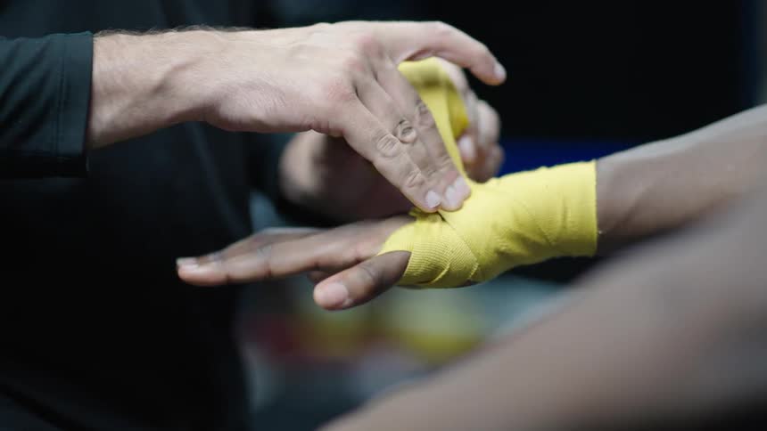 Person putting a yellow ribbon on the hands of a boxer