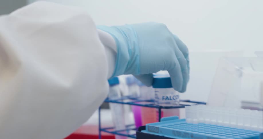 Gloved hand handles laboratory equipment pipetting a sample into a well plate