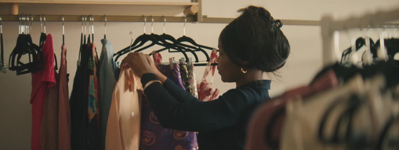 Woman in a Clothing Store Putting a Shirt on a Hanger, Fashion Retail Assistant, Boutique Wardrobe Styling, Garment Display, Store Interior, Shopping Experience, Stylish Outfits, Trendy Dress Selection, Retail Environment, Modern Fashion.