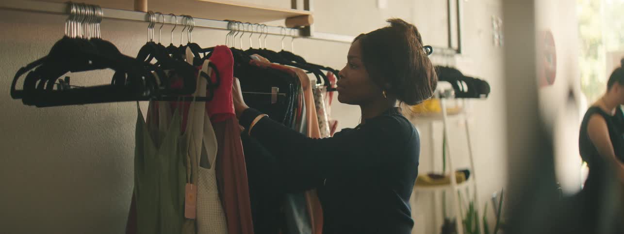 A woman in a clothing store straightens a dress on a rack. Perfect for fashion retail, store display, and wardrobe styling visuals.