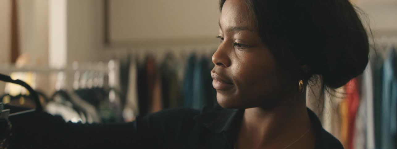 Fashionable woman browsing garments on racks in retail shop.