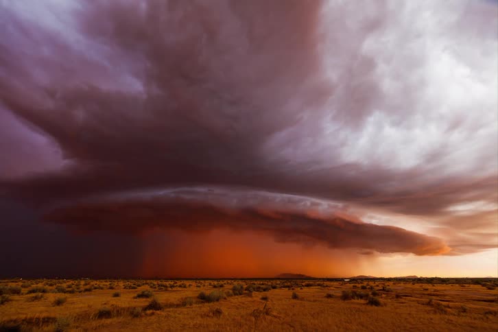 Dark reddish storm clouds hover over a flat landscape