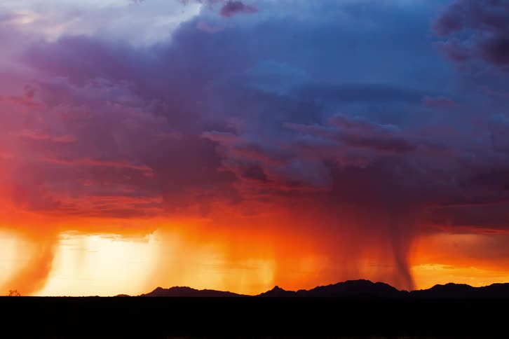 An orange sunset sky with dark clouds passing quickly