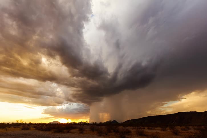 A dense thundercloud passing quickly over a desert region in an orange sky