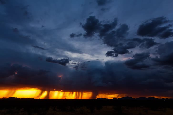 Dramatic sky with dark clouds above and an intense orange light on the horizon