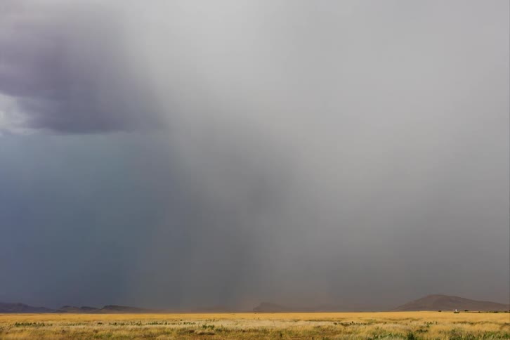 Dark storm clouds with heavy rain hover over a flat landscape
