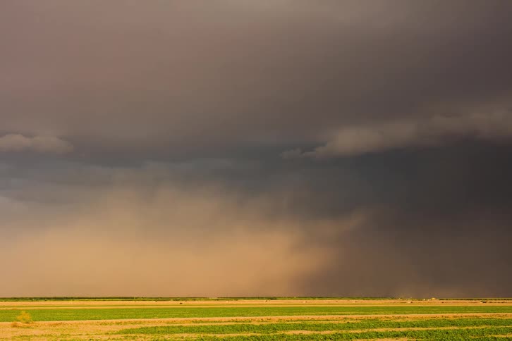 Vast flat landscape under a dramatic sky with dark storm clouds of heavy rain and dust