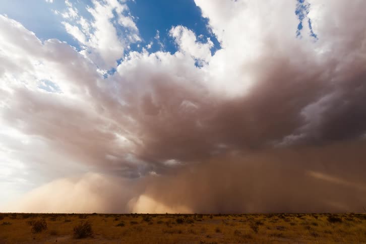 Vast desert landscape under a dramatic sky with a dense dust storm