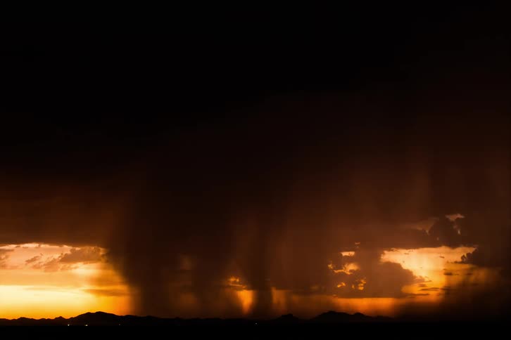 A huge stormy black denunciations and lightning in an orange sky that is darkening