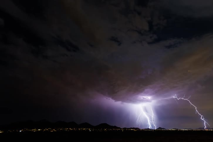 A storm of many clouds with lightning falling in a city in a night