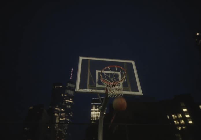 Shirtless man throwing the ball into the basketball hoop on a court at night