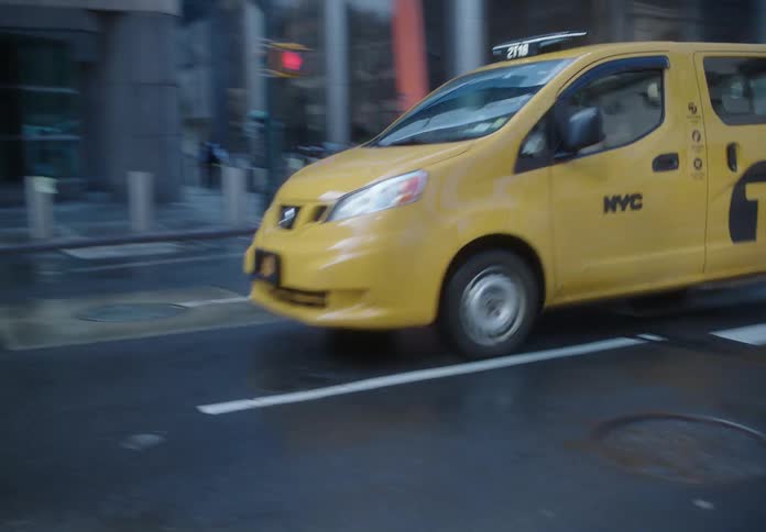 Taxis drive along a downtown street passing intersections and pedestrians