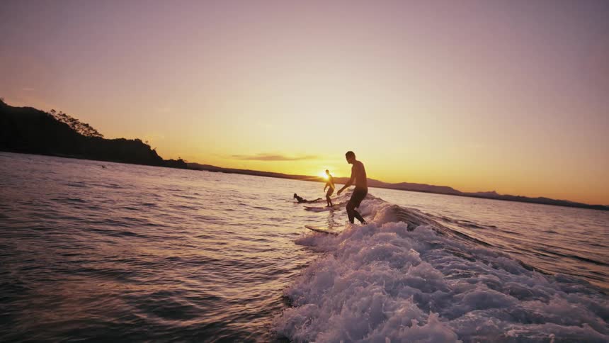 People in the sea surfing waves at sunrise with the sun on the horizon
