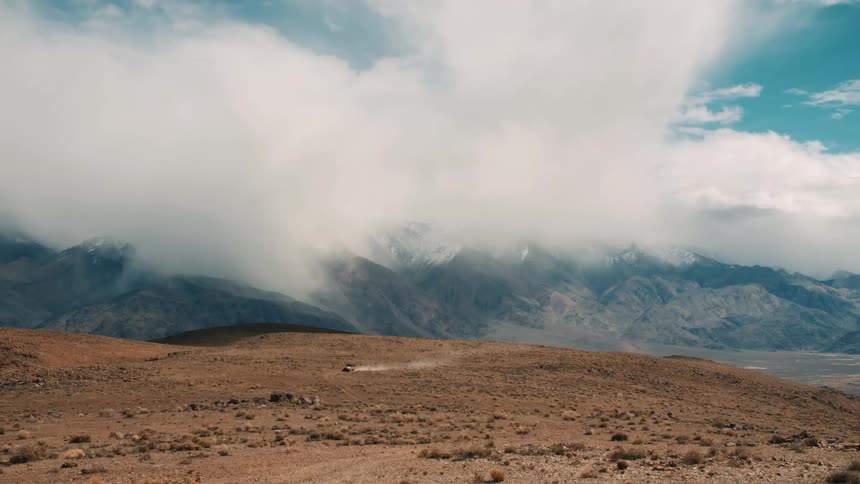 A vehicle drives across a vast desert landscape with a dramatic storm cloud looming overhead