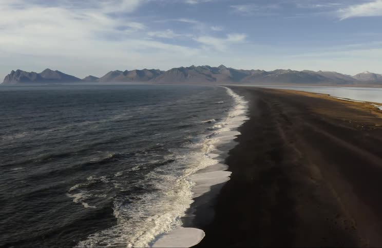 Aerial of ocean waves rolling in to a beach with black sand
