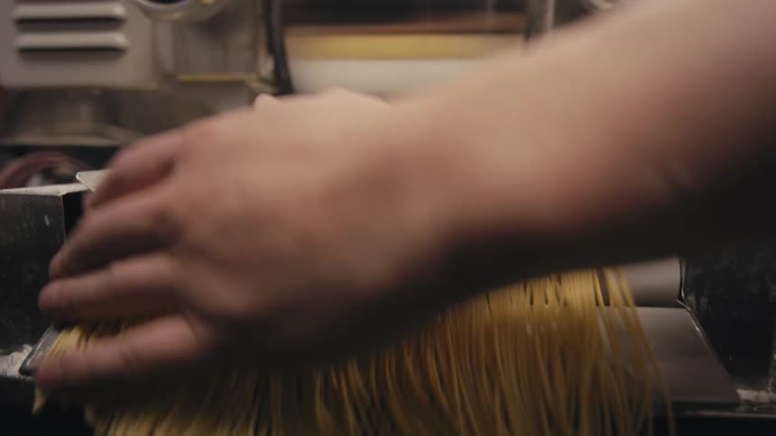 A hand gathers fresh pasta strands from a machine