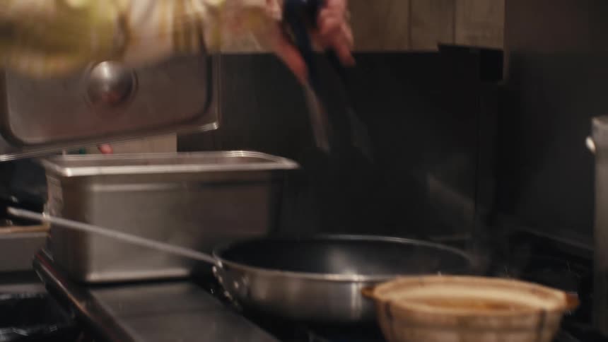 Chef pulling meat from a container and placing it in frying pan