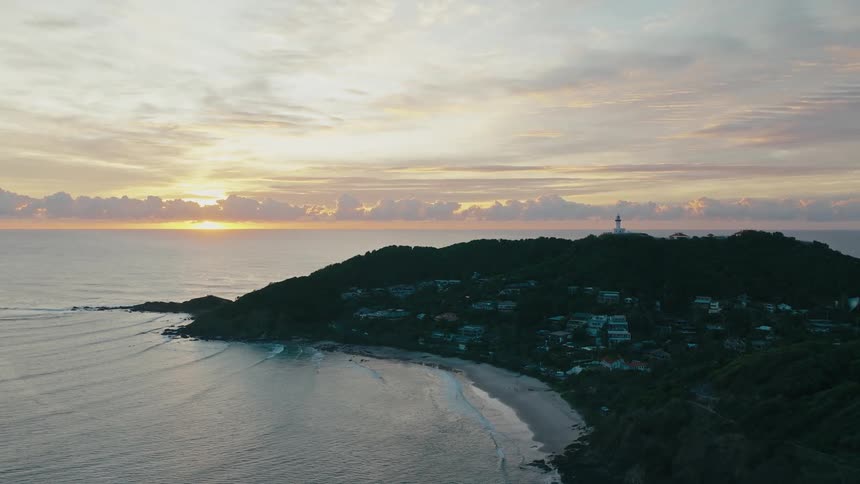 Aerial view of an island with housing surrounded by the sea and a golden sunrise on the horizon